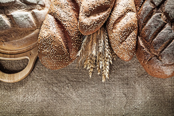 Chopping board brown bread baguette rye ears on burlap backgroun