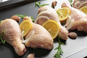 Fresh chicken legs with lemon on baking tray, closeup