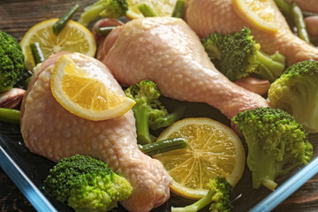 Fresh chicken legs with lemon and broccoli in baking dish, closeup