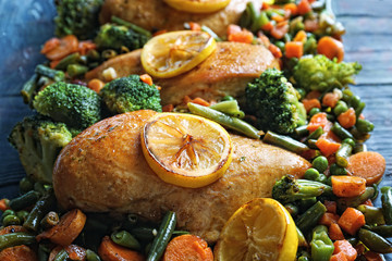 Delicious chicken breasts with lemon and vegetables in baking dish, closeup