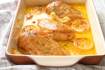 Delicious chicken breasts with lemon in baking dish on table