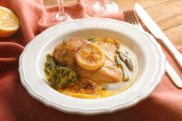 Delicious chicken breast with lemon and vegetables in plate on table