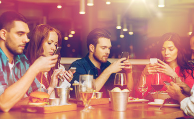 friends with smartphones dining at restaurant