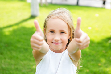 Happy little girl showing thumbs up  outdoors in summer day.