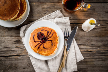 Ideas for breakfast are Halloween, food for children. Pumpkin pie pancakes decorated with chocolate syrup in a traditional style - spider web, spider, jack lantern. On wooden rustic table, copy space