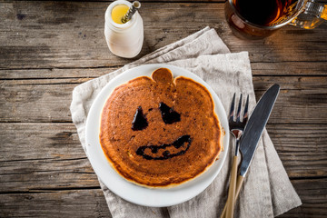Ideas for breakfast are Halloween, food for children. Pumpkin pie pancakes decorated with chocolate syrup in a traditional style - spider web, spider, jack lantern. On wooden rustic table, copy space