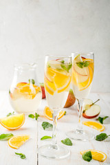 Drinks and cocktails. White autumn sangria with apples, orange, mint and white wine. In glasses for champagne, in a pitcher, on a white wooden table. Copy space