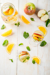 Drinks and cocktails. White autumn sangria with apples, orange, mint and white wine. In glasses for champagne, in a pitcher, on a white wooden table. Copy space top view