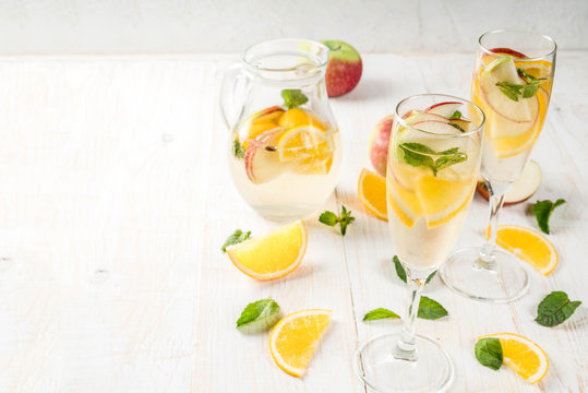 Drinks and cocktails. White autumn sangria with apples, orange, mint and white wine. In glasses for champagne, in a pitcher, on a white wooden table. Copy space