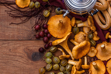 orange chanterelle mushrooms, yellow and red gooseberries, samovar, bagels and patterned scarf on brown wooden table