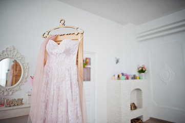 Beautiful wedding dress hanging on the rack in the middle of big white room.