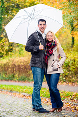 Couple enjoying fall day having walk despite the rain, the foliage is colorful