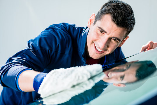 Cheerful young male worker polishing car with white soft microfiber mitt at auto wash