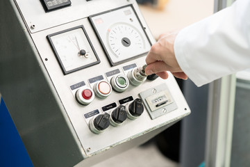 Close-up of the hand of a woman wearing white lab coat while turning on an industrial machine, with mechanical key-operated switch during work in a factory