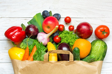 Full paper bag of different fruits and vegetables on a white wooden background