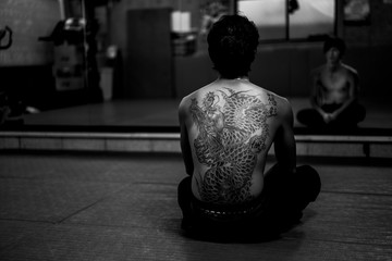 Black and white portrait of a heavily tattooed Japanese man watching himself in a big mirror