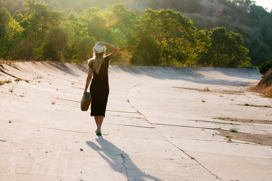 Woman with a black dress walking her back to the camera with the sunset