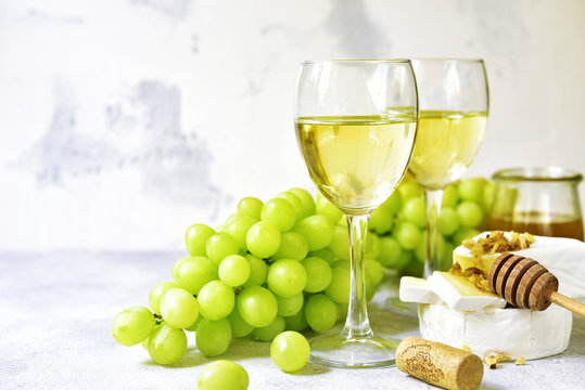 Two glasses of white wine,cheese and grapes.