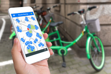 Bicycle sharing service or rental technology concept. Sharing economy and collaborative consumption. Customer hand using mobile phone to find bicycle for ride.