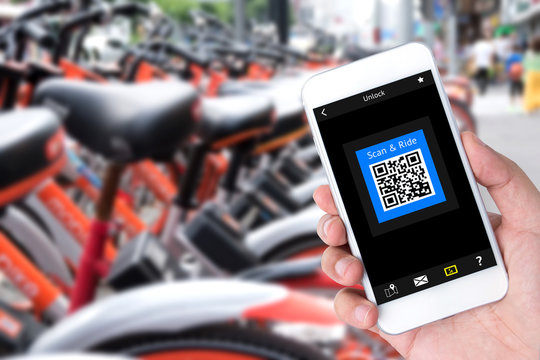 Bicycle sharing service or rental technology concept. Sharing economy and collaborative consumption. Customer hand using mobile phone to qr code application for ride bicycle.
