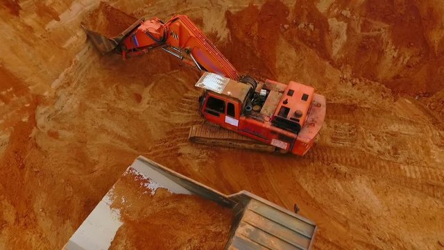 View from above of mining excavator pouring sand in dumper truck. Crawler excavator mining sand in quarry. Sky view of industrial machinery at sand quarry. Mining industry. Dump truck