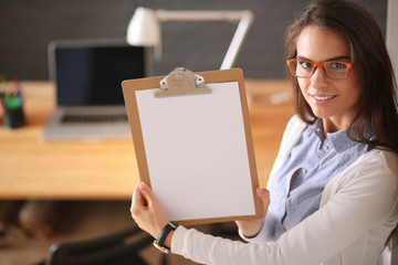 Young woman standing near desk with laptop holding folder and cup of coffee. Workplace. Business...