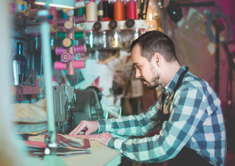 Fototapeta na wymiar male worker sewing stitches on belt in leather workshop