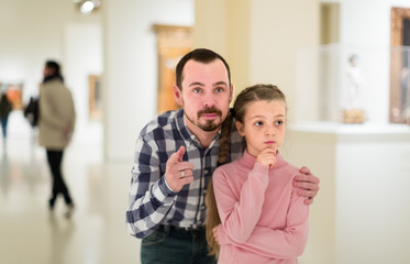 Smiling father and daughter regarding paintings in museum