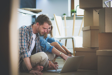 Young couple moving in new home.Sitting and relaxing after unpacking.Looking something on laptop. Young couple