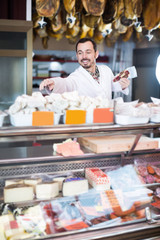 Fototapeta na wymiar Smiling male butcher showing sorts of meat