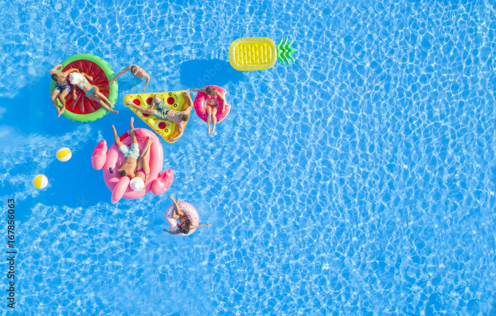 Wall mural AERIAL TOP DOWN COPY SPACE Fit girls and muscular guys lying on colorful floaties in pool, relaxing and hanging out on the sun. Friends on fun summer vacation floating on water on inflatable pillows