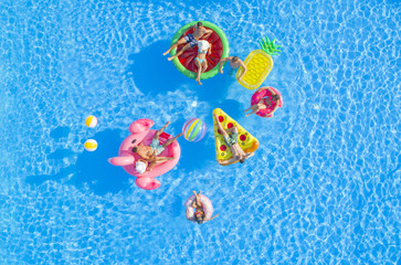 AERIAL TOP DOWN COPY SPACE Fit girls and muscular guys lying on colorful floaties in pool, relaxing...