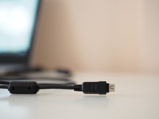 Black camera-USB connector with cable and laptop in the background