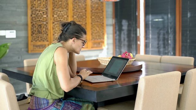 Woman having problem with laptop while sitting in the dining room, steadycam shot
