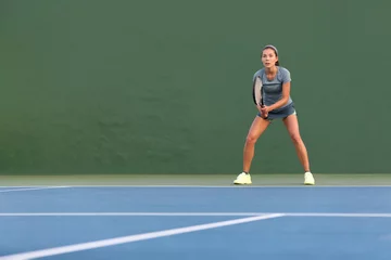 Wandaufkleber Tennis player woman standing ready to play waiting to receive serve. Outdoor fitness instructor focused playing on hard court on green background. © Maridav