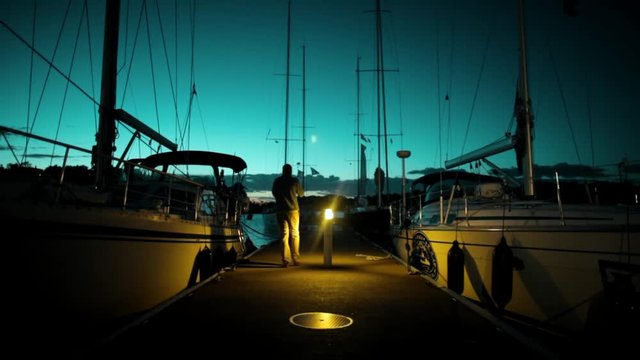 Yachts and boats in old port in mediterranean sea at night, sunset, man goes