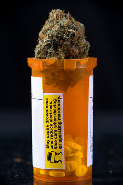 Detail of cannabis buds sitting on a prescriptions pills bottle over black background