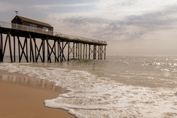 Fishing pier stands tall as waves flow gently towards the shore on a sunny morning