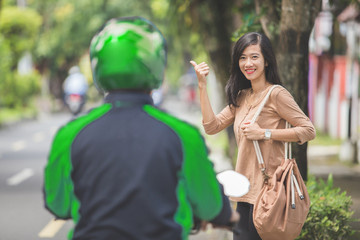 woman standing on sidewalk ordering motorcycle taxi by waving her hand