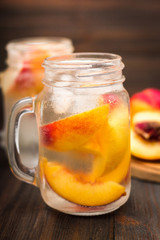 Mason jar glass of homemade peach iced water on a rustic wooden background.