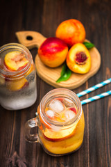 Mason jar glass of homemade peach iced water on a rustic wooden background.
