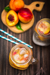 Mason jar glass of homemade peach iced water on a rustic wooden background. Top view.