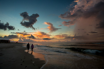 Mother and daughter walk down a beach at sunrise