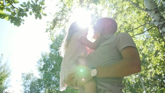 Happy father hugging and swinging his daughters in park, slow-motion