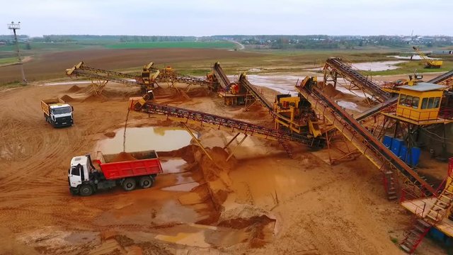 View from above mining conveyor working on sand mine. Mining conveyor pour sand in dumper truck. Mining equipment on industrial park. Aerial view of mining machinery on sand quarry
