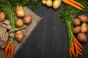 Fresh carrots and potatoes on a black wooden background. rustic style
