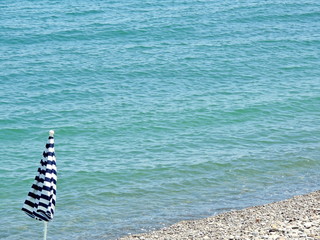 Closed beach umbrella on the beach. Marine background with copy space for text.