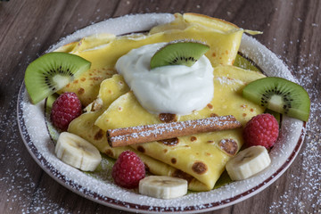 Homemade pancake with vanilla curd, raspberries, kiwi and banana pieces sprinkled with cocoa