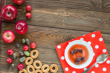 ripe red apples, actinidia berries, bagels, strawberry jam in white saucer, spoon, red napkin at white polka dots on wooden table, top view