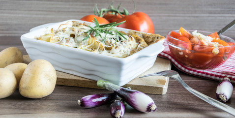Baked potatoes with cream, rosemary and oyster sauce in a white frying pan and on a wooden cutting board